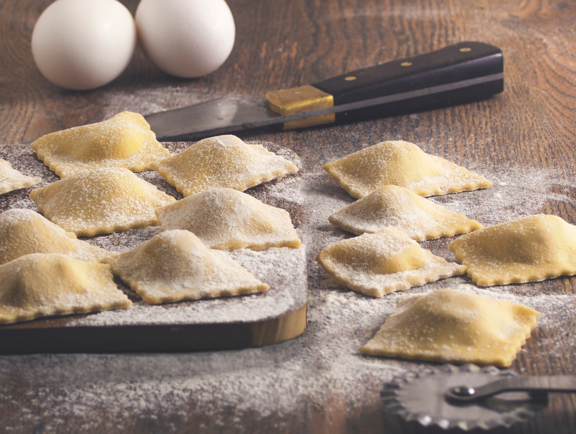 Uncooked chicken and vegetable ravioli on floured surface, pinched edges