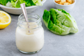 Caesar dressing jar with spoon, creamy pale dressing in clear glass container