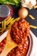 Bolognese sauce on a wooden spoon over a bowl of tomato-based sauce