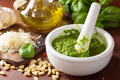 Basil pesto sauce in a white bowl with fresh green leaves
